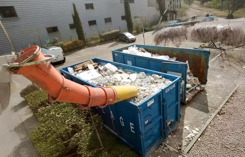 Chantier extérieur de démolition avec bennes à gravats bleues remplies de débris de construction blancs et matériaux de démolition