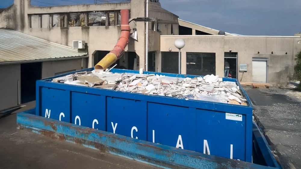 Scène extérieure d'un chantier de démolition avec une benne bleue remplie de gravats et débris de construction