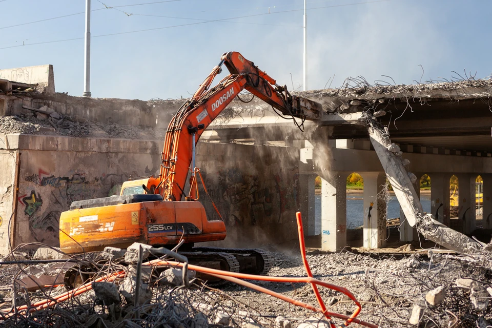 Chantier de démolition en extérieur avec pelleteuse hydraulique orange Doosan 255LCV équipée d'un brise-roche hydraulique détruisant une structure en béton armé