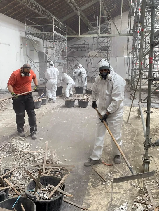 Atelier de métallurgie industrielle où un ouvrier utilise une meuleuse d'angle sur une structure métallique tubulaire